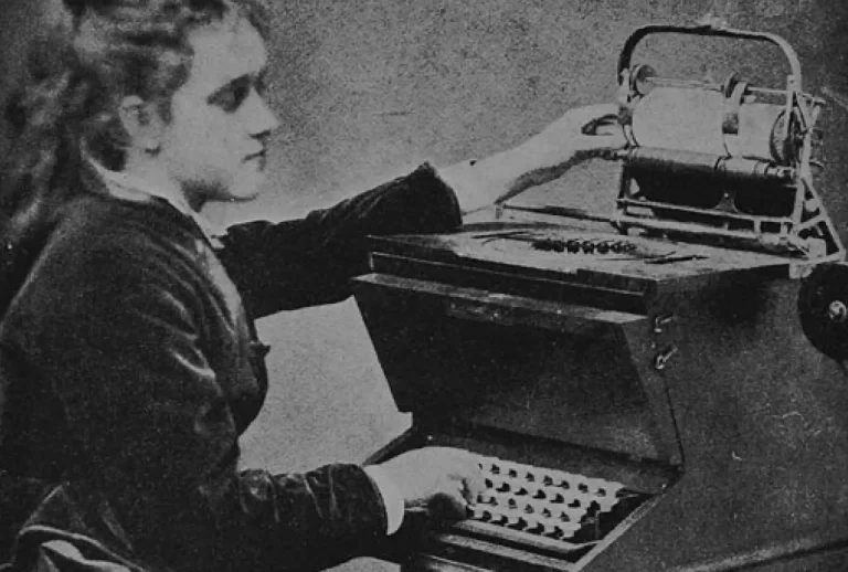 A máquina de escrever e o design de 2026: Por que menos é, de facto, mais. Mulher sentada a operar uma máquina de escrever antiga, ilustrando o conceito de design funcional e foco na utilidade essencial.